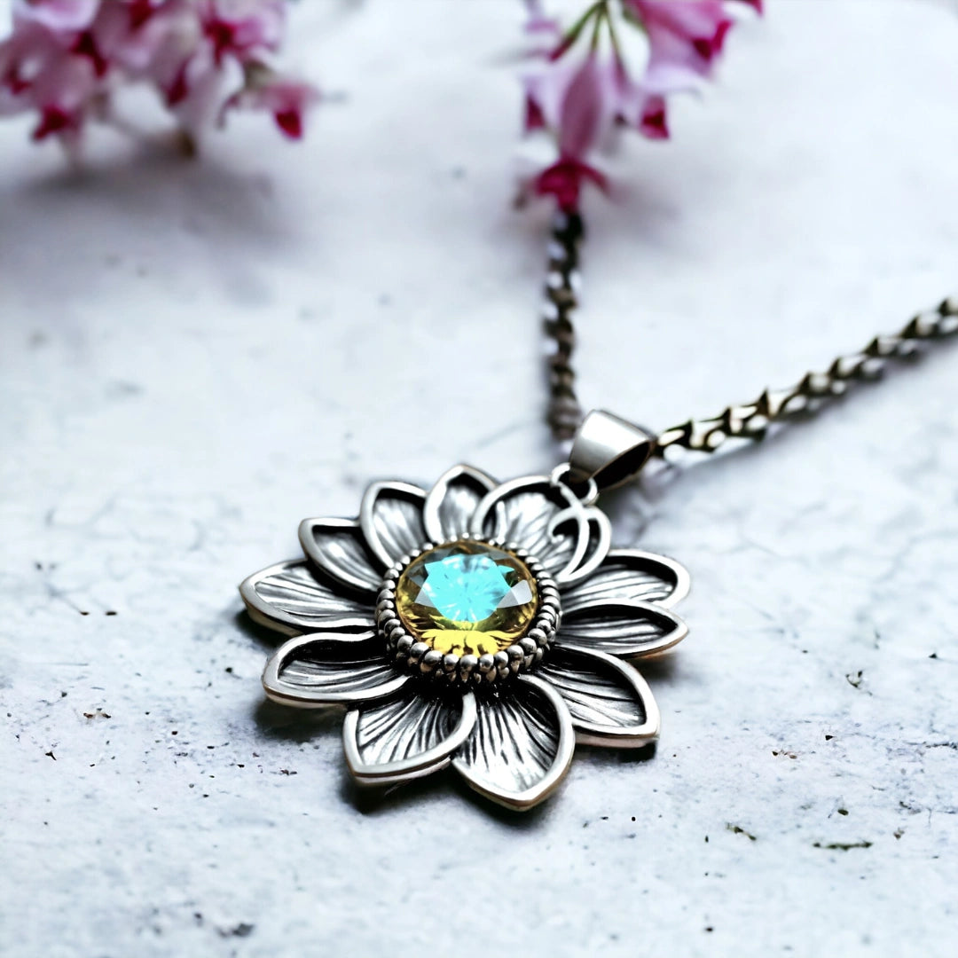 Helios Sunburst Amber Pendant Necklace for Everyday Wear featuring a silver-tone flower pendant with an ocean blue gemstone centre and a detailed, handcrafted, coastal-inspired design on a necklace chain.