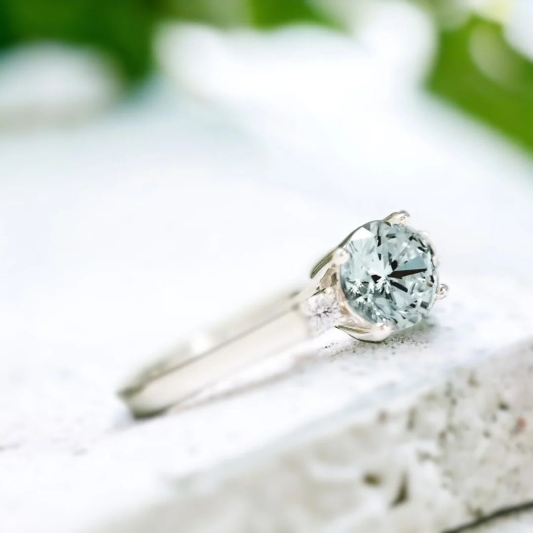 Lab-Created Diamond Aquamarine Trilogy Ring Engagement Design featuring a round 1.15 Ct aquamarine centre stone with a vibrant blue hue, flanked by lab-created white diamond side stones in a balanced trilogy setting with a slim straight shank design.