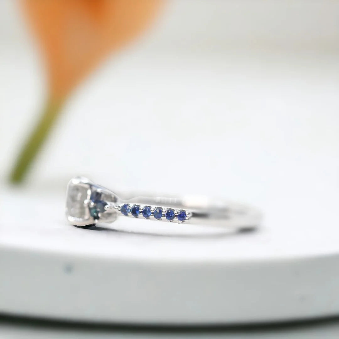 Milky Way Diamond Ring Mossy Glen Engagement Ring Statement Ring featuring a round salt-and-pepper diamond center stone with soft milky grey tones, accented by blue marquise and round gemstones in a slim modern engagement ring design