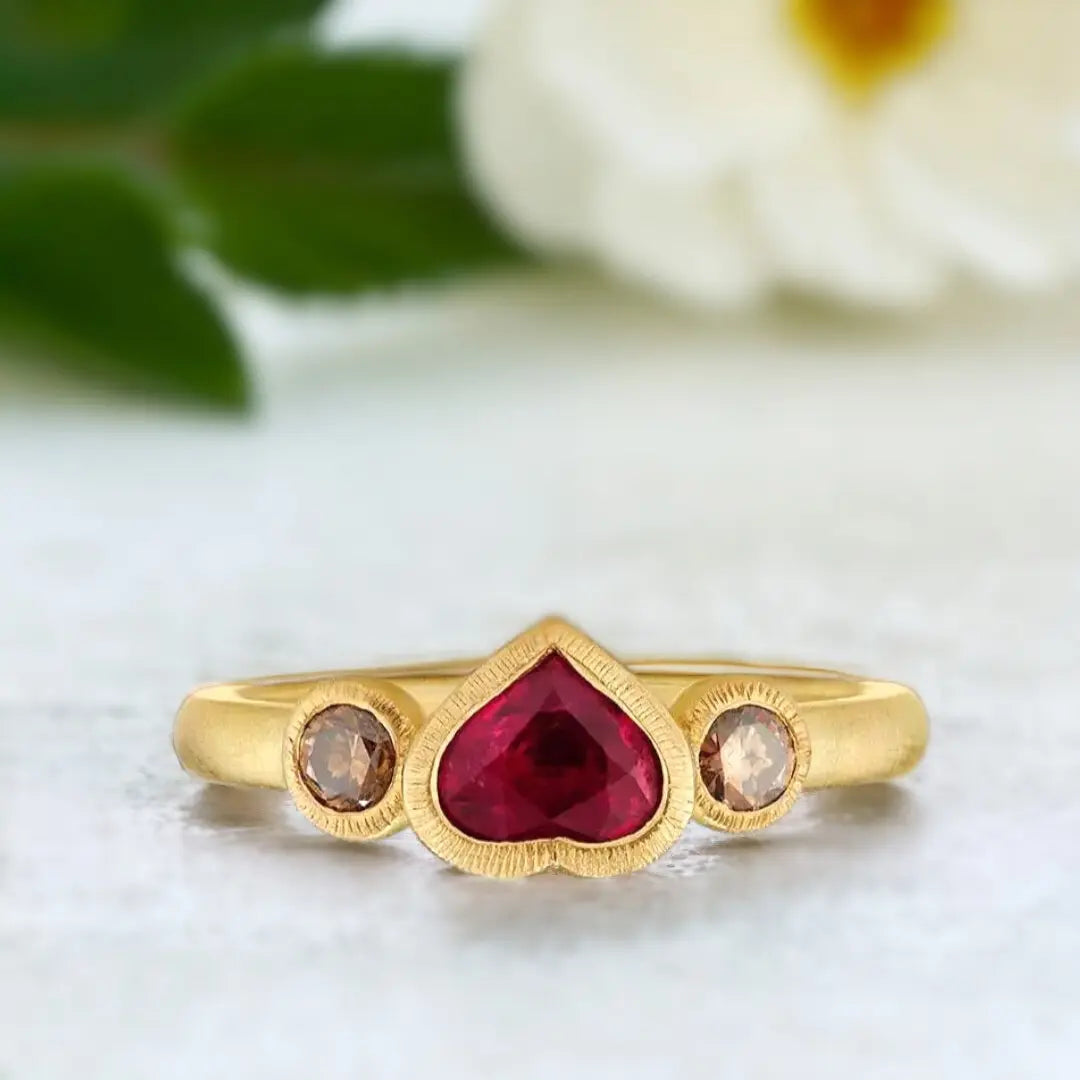 Ruby Heart Ring: Heart-shaped ruby ethical handmade design featuring a natural heart-shaped ruby centre stone with rich red colour, round brown diamond accents, and a slim straight band in a polished handmade setting.